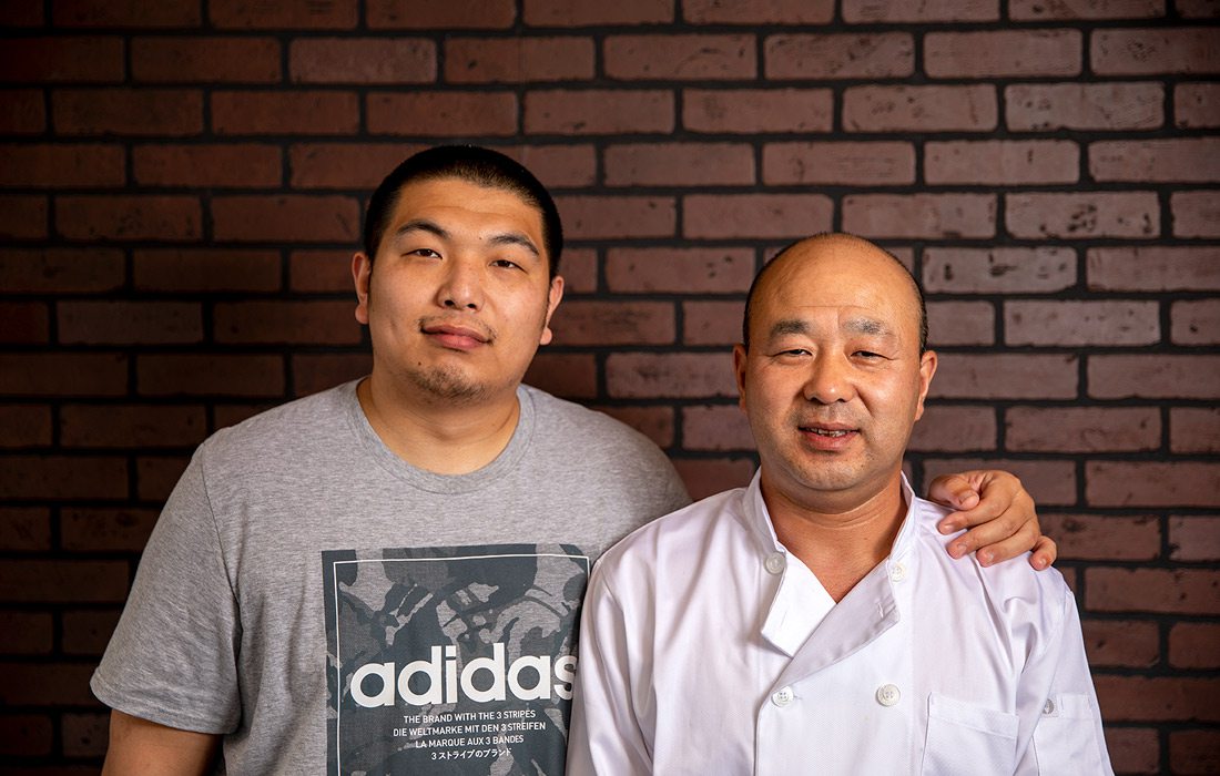 Father and son stand in front of brick wall