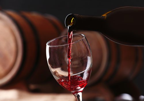 Red wine is poured into a glass against a background of stacked barrels.
